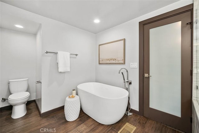 bathroom with visible vents, baseboards, toilet, wood finished floors, and a freestanding tub