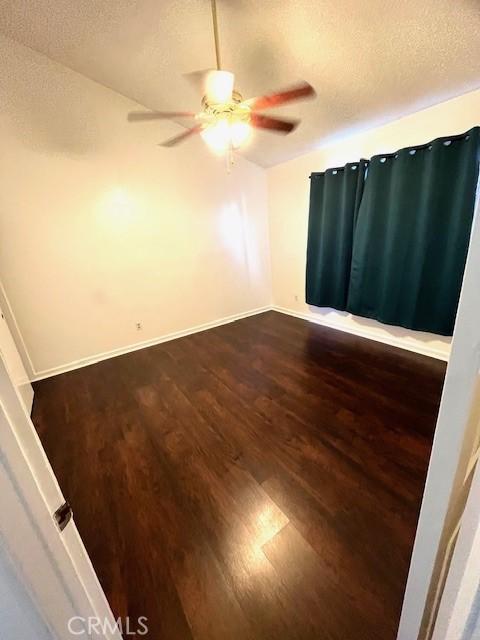 spare room with dark wood-type flooring, a ceiling fan, baseboards, and a textured ceiling