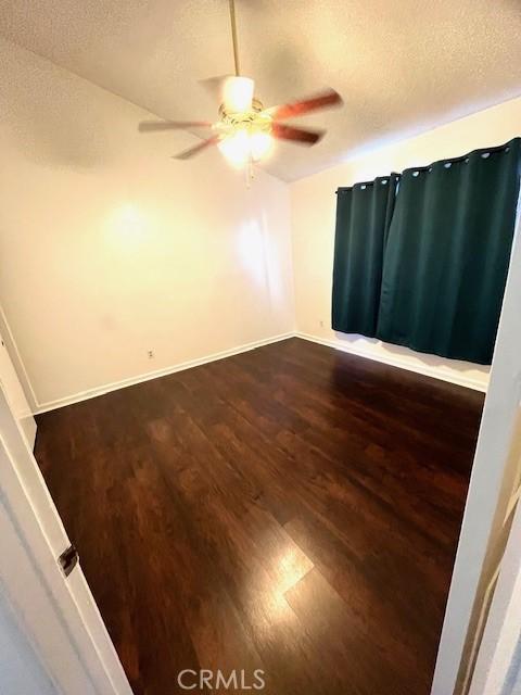 unfurnished room with a ceiling fan, a textured ceiling, dark wood-style floors, and baseboards