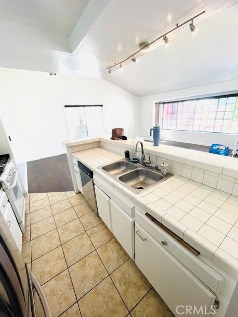 kitchen featuring light tile patterned floors, a sink, tile counters, white cabinetry, and stainless steel dishwasher