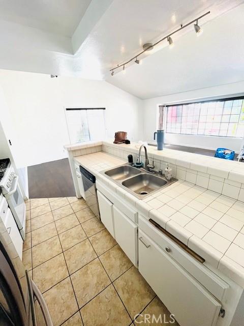 kitchen featuring white cabinets, light tile patterned flooring, a sink, rail lighting, and a wealth of natural light