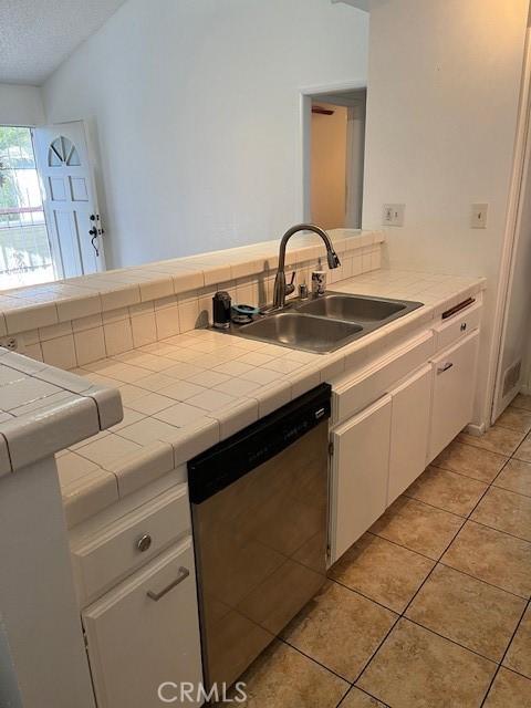 kitchen featuring tile countertops, stainless steel dishwasher, a sink, light tile patterned floors, and white cabinetry
