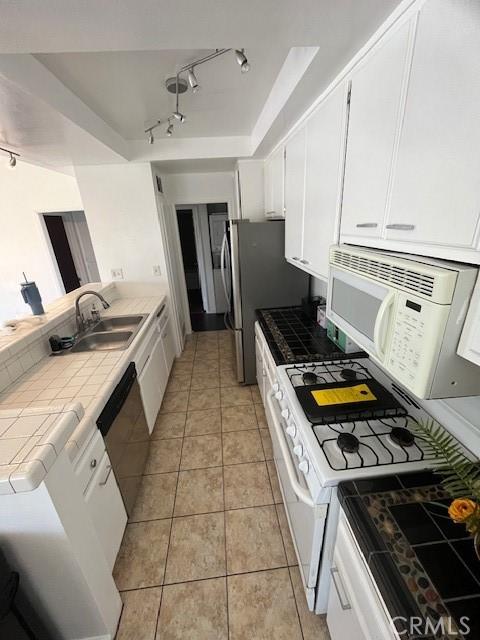 kitchen featuring a sink, white cabinets, stainless steel appliances, and tile counters