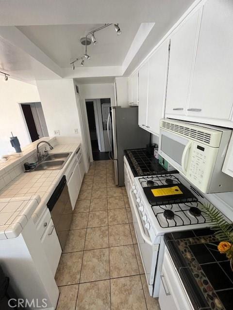 kitchen featuring appliances with stainless steel finishes, a sink, tile counters, rail lighting, and white cabinetry