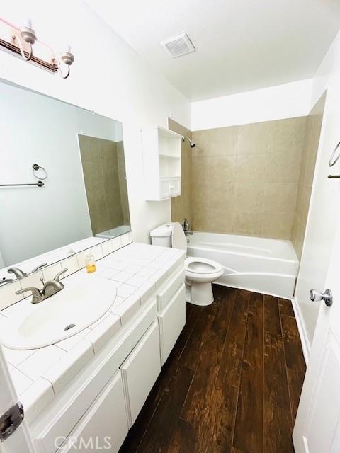 bathroom with visible vents, toilet, shower / bathing tub combination, wood finished floors, and vanity