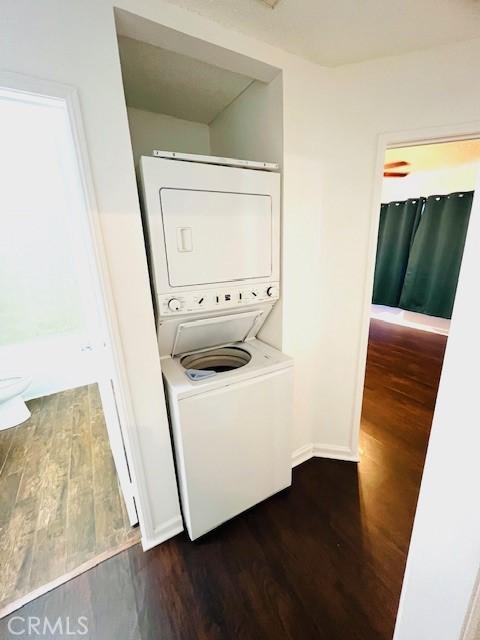 laundry area with baseboards, laundry area, dark wood-style flooring, and stacked washing maching and dryer