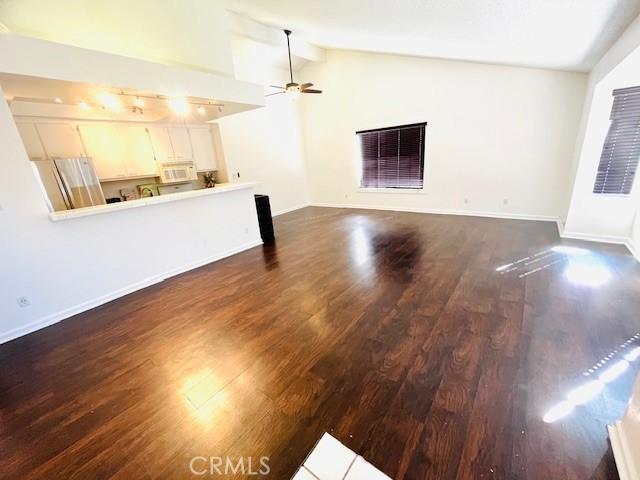 unfurnished living room featuring dark wood-style flooring, a ceiling fan, baseboards, and lofted ceiling
