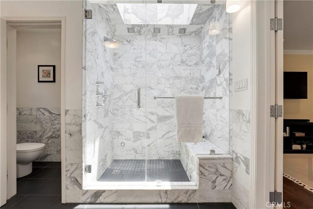 bathroom featuring a marble finish shower, toilet, tile walls, and ornamental molding