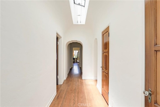 hallway featuring arched walkways, baseboards, and light wood-style floors