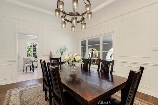 dining room with a notable chandelier, dark wood finished floors, crown molding, and a decorative wall