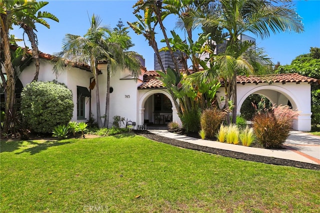 mediterranean / spanish-style home with stucco siding, driveway, a front lawn, and a tile roof