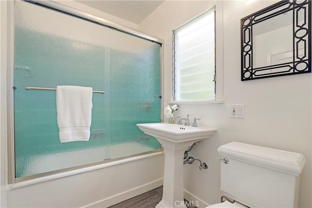 full bath with plenty of natural light, toilet, wood finished floors, and shower / bath combination with glass door