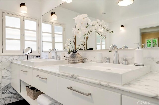 bathroom with double vanity, marble finish floor, tile walls, and a sink