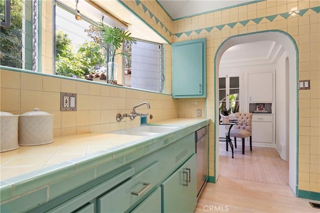 interior space with green cabinets, tile counters, dishwasher, arched walkways, and a sink