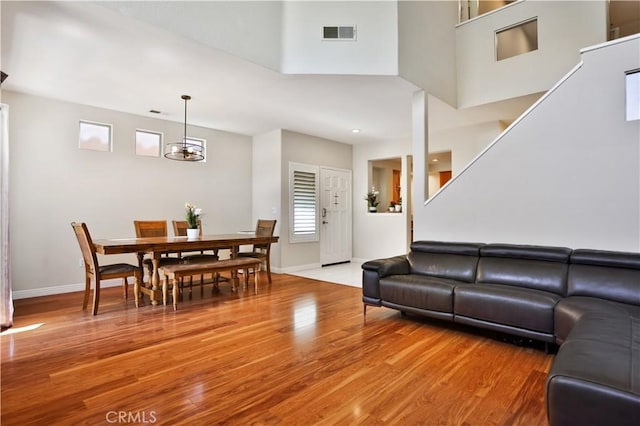 living area with visible vents, baseboards, wood finished floors, an inviting chandelier, and a towering ceiling