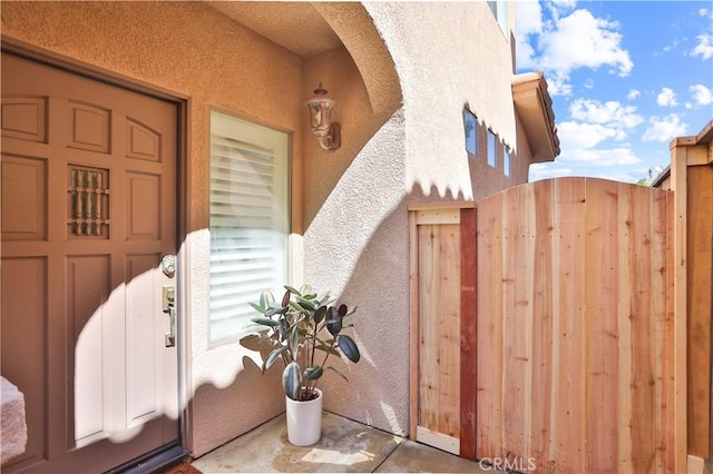 view of exterior entry with a gate and stucco siding