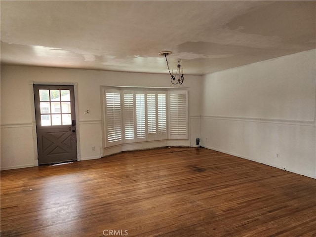 unfurnished dining area featuring a notable chandelier, wood finished floors, and wainscoting