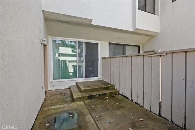 doorway to property featuring stucco siding and fence