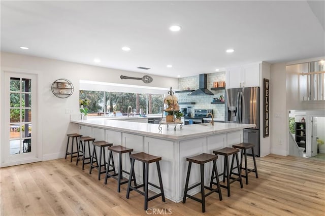 38680 Mesa Rd, Temecula, CA 92592 - kitchen featuring appliances with stainless steel finishes, wall chimney range hood, tasteful backsplash, white cabinets, and light wood-type flooring