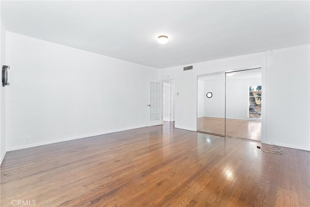 unfurnished bedroom with a closet, baseboards, visible vents, and wood finished floors