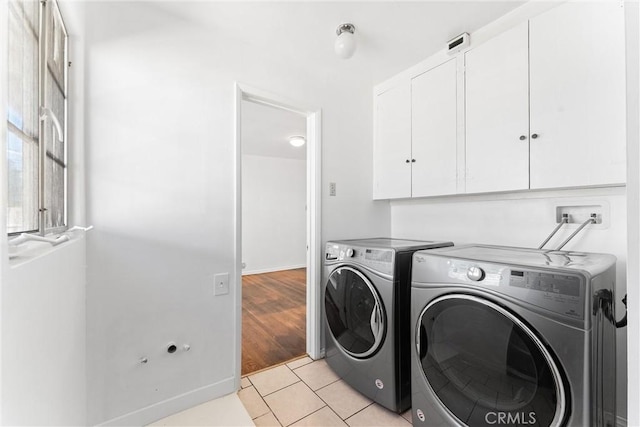 clothes washing area with washing machine and dryer, light tile patterned floors, and cabinet space