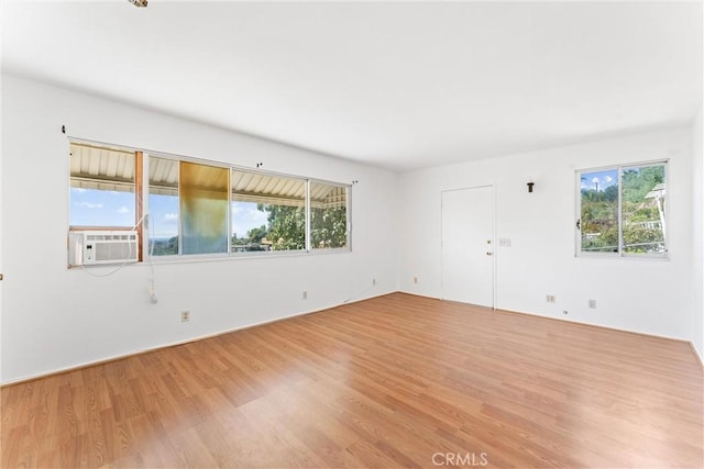 empty room with a wealth of natural light, cooling unit, and light wood finished floors