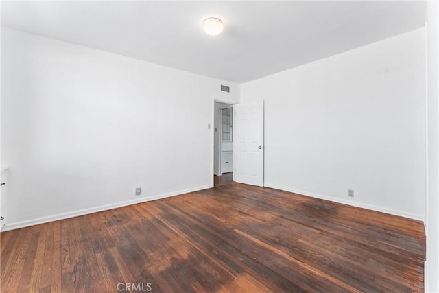 spare room featuring visible vents, baseboards, and dark wood-style flooring