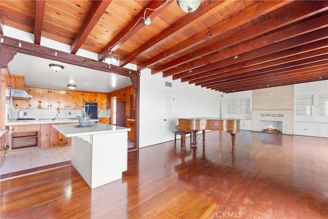 kitchen with light countertops, wood finished floors, under cabinet range hood, and beam ceiling