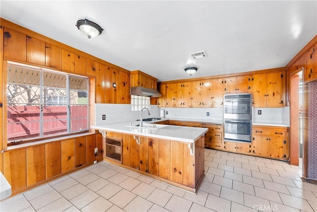 kitchen with visible vents, a peninsula, under cabinet range hood, double oven, and brown cabinets