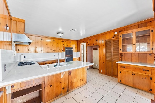 kitchen with gas cooktop, stainless steel double oven, a peninsula, light countertops, and under cabinet range hood