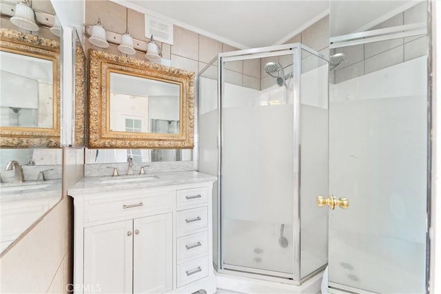 bathroom featuring a shower stall, ornamental molding, two vanities, and a sink