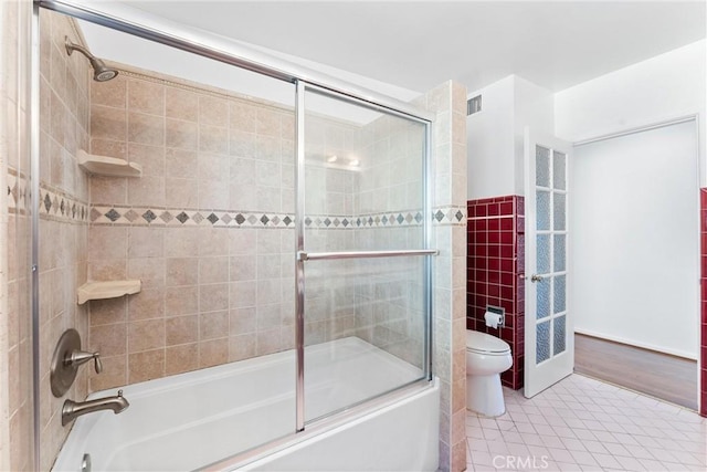 bathroom featuring visible vents, toilet, shower / bath combination with glass door, tile patterned floors, and tile walls