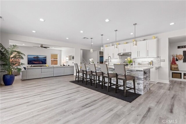 kitchen with a breakfast bar, white cabinets, light wood-style floors, under cabinet range hood, and backsplash