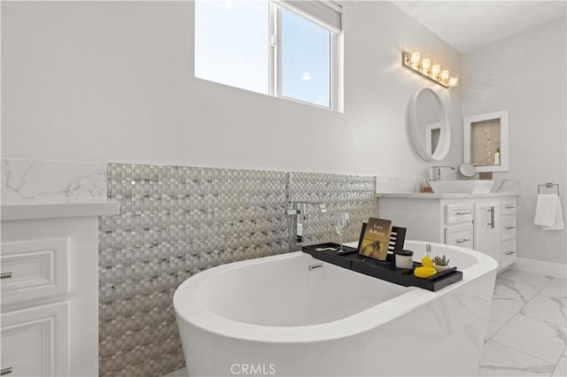 full bath featuring tile walls, a soaking tub, marble finish floor, and vanity