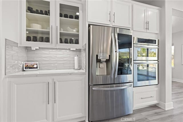 kitchen with decorative backsplash, white cabinets, appliances with stainless steel finishes, and glass insert cabinets