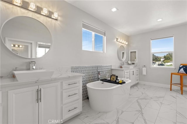 bathroom with baseboards, two vanities, a soaking tub, marble finish floor, and a sink