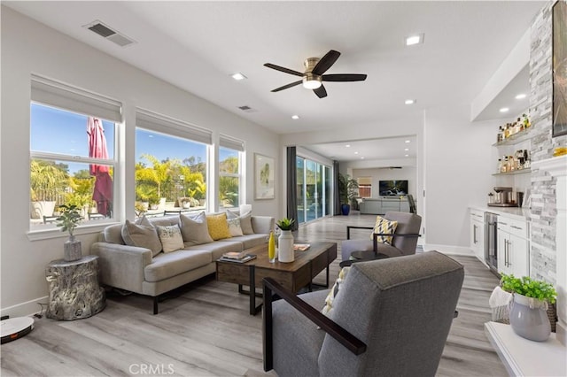 living area featuring visible vents, a ceiling fan, light wood-style floors, a bar, and baseboards