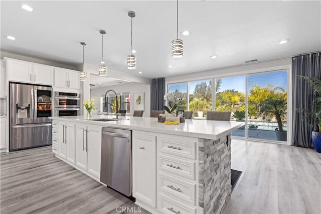 kitchen featuring visible vents, light wood-style flooring, a kitchen island with sink, a sink, and appliances with stainless steel finishes