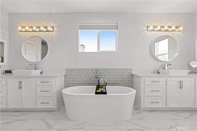 full bath with a sink, a freestanding bath, marble finish floor, and two vanities