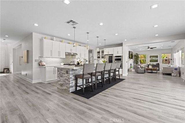 kitchen with under cabinet range hood, open floor plan, a large island, and white cabinets