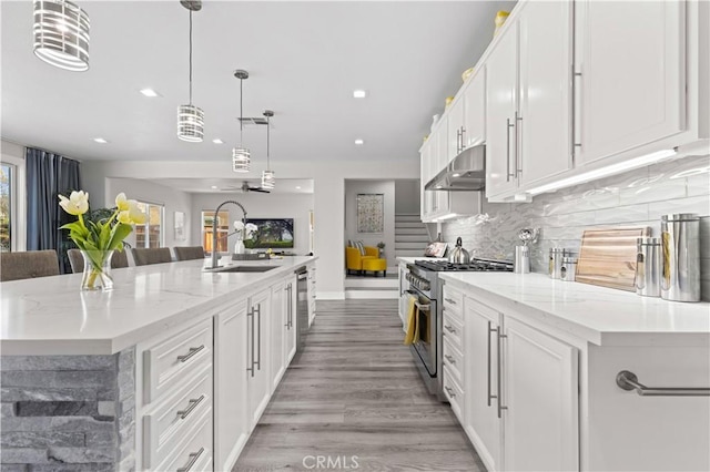 kitchen featuring a sink, decorative backsplash, stainless steel range, under cabinet range hood, and white cabinetry