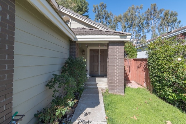 view of exterior entry featuring brick siding and fence