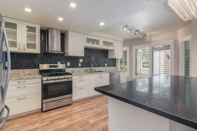 kitchen featuring wall chimney range hood, appliances with stainless steel finishes, light wood-style floors, white cabinetry, and a sink