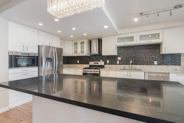 kitchen with light wood-type flooring, a sink, backsplash, appliances with stainless steel finishes, and wall chimney exhaust hood