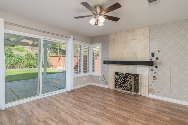 unfurnished living room with a ceiling fan, wood finished floors, visible vents, baseboards, and wallpapered walls