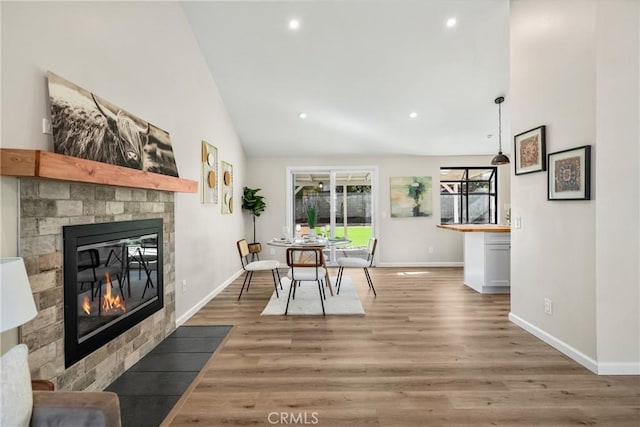 dining room featuring baseboards, light wood-style flooring, a fireplace with flush hearth, recessed lighting, and vaulted ceiling