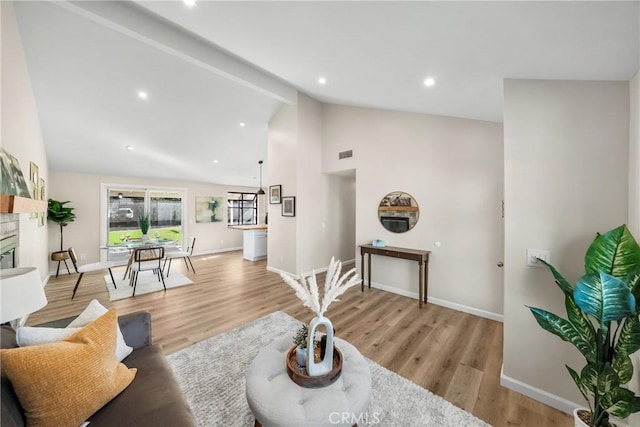 living room with visible vents, baseboards, beam ceiling, light wood-style floors, and a glass covered fireplace