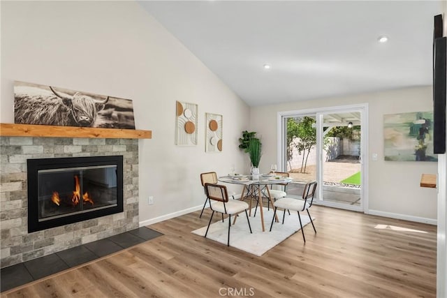 dining area with baseboards, high vaulted ceiling, wood finished floors, and a fireplace with flush hearth