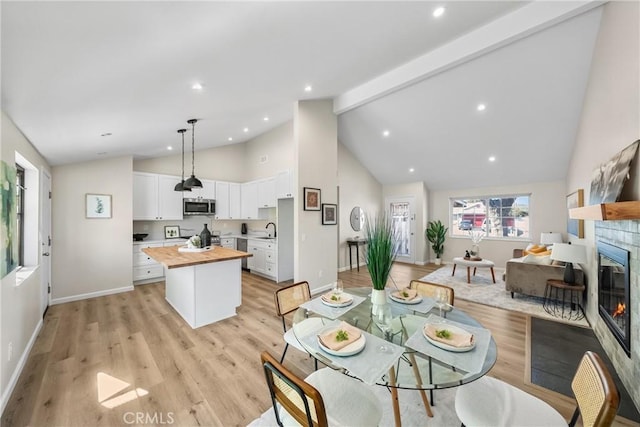 dining area featuring light wood-type flooring, baseboards, beamed ceiling, and a fireplace