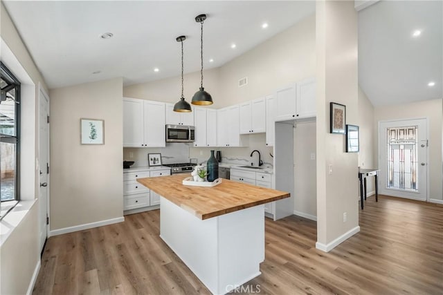 kitchen featuring a sink, appliances with stainless steel finishes, wood counters, white cabinetry, and a center island